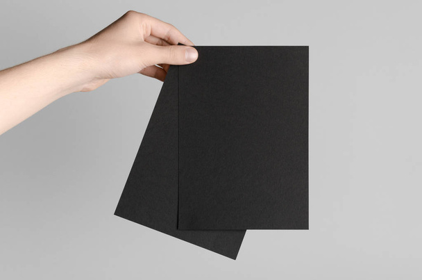 Black A5 Flyer / Invitation Mock-Up - Male hands holding black flyers on a gray background. - Foto, immagini