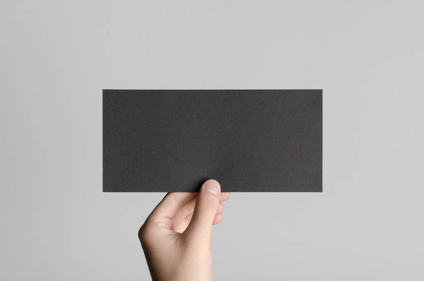 Black DL Flyer Mock-Up - Male hands holding a black flyer on a gray background. - Foto, Imagem