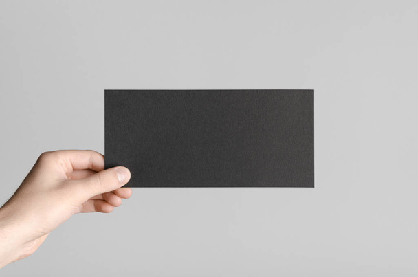 Black DL Flyer Mock-Up - Male hands holding a black flyer on a gray background. - Foto, Bild