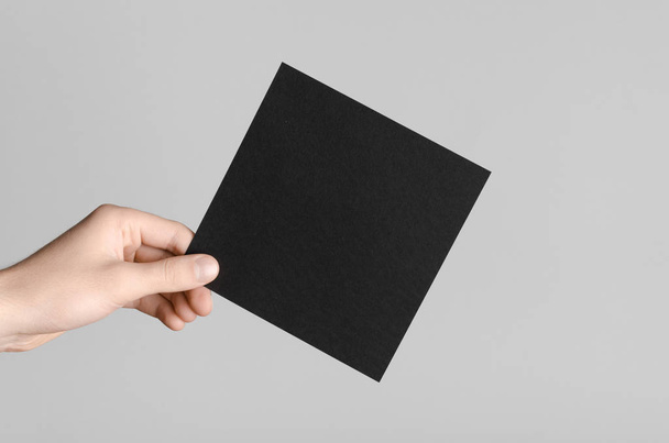 Black Square Flyer / Invitation Mock-Up - Male hands holding a black flyer on a gray background. - Photo, Image