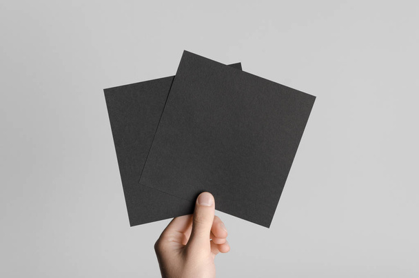 Black Square Flyer / Invitation Mock-Up - Male hands holding black flyers on a gray background. - Photo, Image