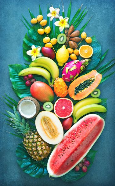 Ассортимент тропических фруктов с пальмовыми листьями и экзотическими цветами. Вид сверху
 - Фото, изображение
