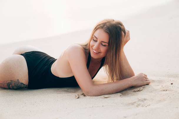 close-up of a beautiful happy young girl of European appearance resting on the lap. The model lies on the sand, wears a fashionable apron and laughs cheerfully, closing your eyes with pleasure. - Foto, afbeelding