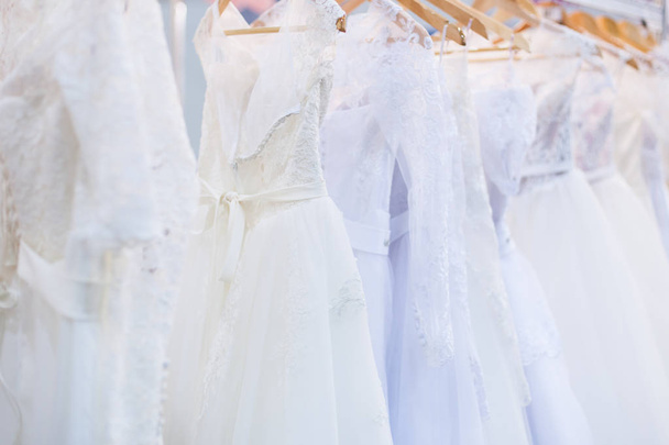 Beautiful white wedding dresses hang on the counter in the store. - Фото, изображение