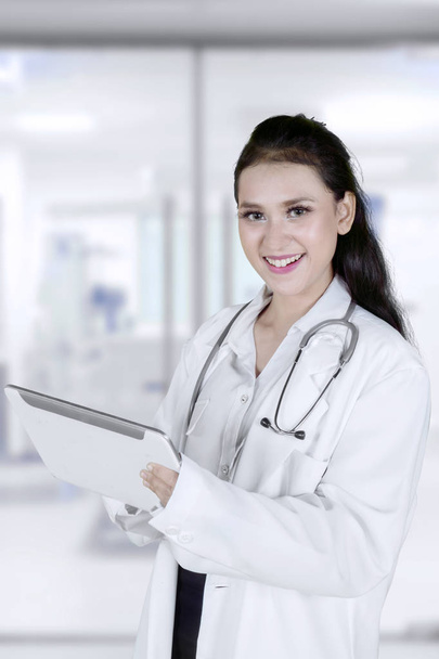 Portrait of beautiful physician smiling at the camera while holding a digital tablet and standing in the hospital - Photo, image