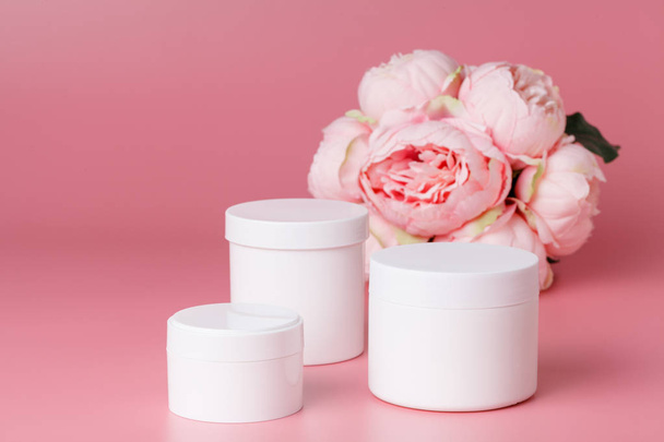 Cosmetic cream container and pink flowers on pink plaint  background - 写真・画像