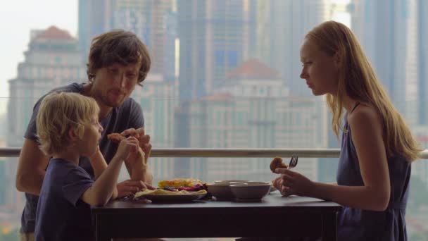 Jong gezin met een ontbijt, lunch op hun balkon in een wolkenkrabber met uitzicht op een hele centrum van de stad - Video