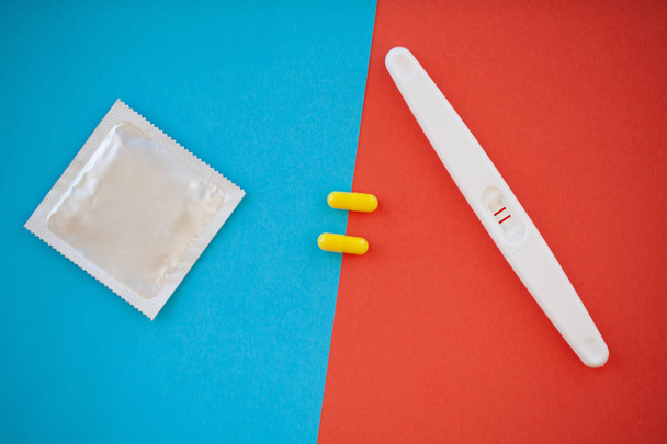 Schwangerschaftstest. das Ergebnis ist positiv mit zwei Streifen und Kondom mit Verhütungsmittel auf farbigem Hintergrund, Antibabypille, Safe Sex, Gesundheitskonzept. - Foto, Bild