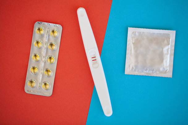 Zwangerschapstest. Het resultaat is positief met twee strips en condoom met anticonceptiva op gekleurde achtergrond pil van de Geboortenbeperking, veilige seks, gezondheidszorg concep. - Foto, afbeelding