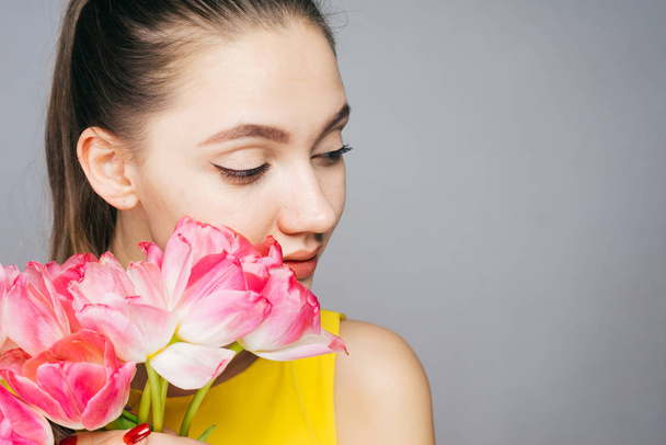 charming young girl in yellow dress posing, holding fragrant pink flowers - 写真・画像