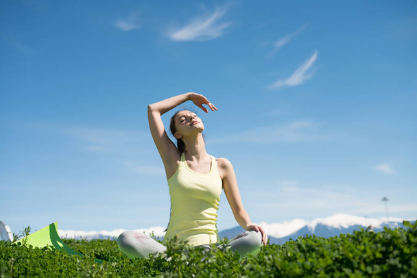 a peaceful young woman meditating and practicing yoga in the park in the sun, closed her eyes - Photo, image