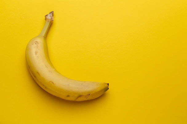 Single banana fruit isolated on yellow background - Foto, Imagen