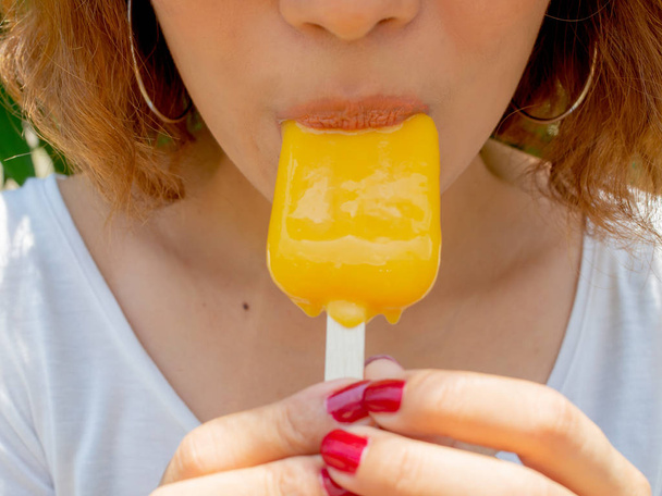 Gyönyörű nő rövid haj visel fehér ing boldog mosolygó gazdaság és étkezés sárga Bited Popsicle Ice Pop nyáron a napsütés, a fa háttér - Fotó, kép
