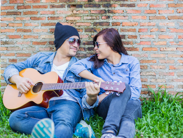 Hipster-Mann spielt Gitarre für seine Freundin im Freien gegen Ziegelwand und genießt zusammen. - Foto, Bild
