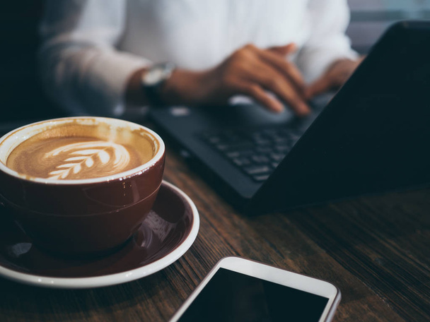 Handtippen auf schwarzem Laptop mit Computermaus, konzentriert bei der Arbeit mit Kaffee und Handy auf dem Holztisch im Café. Arbeitsfrauenkonzept. - Foto, Bild