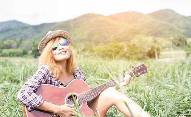 Joven chica hipster sentada tocando una guitarra y cantando
. - Foto, imagen