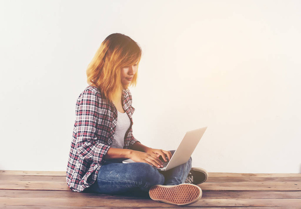 Mulher jovem hipster sentado no chão de madeira com pernas cruzadas e usando laptop no fundo branco
 - Foto, Imagem