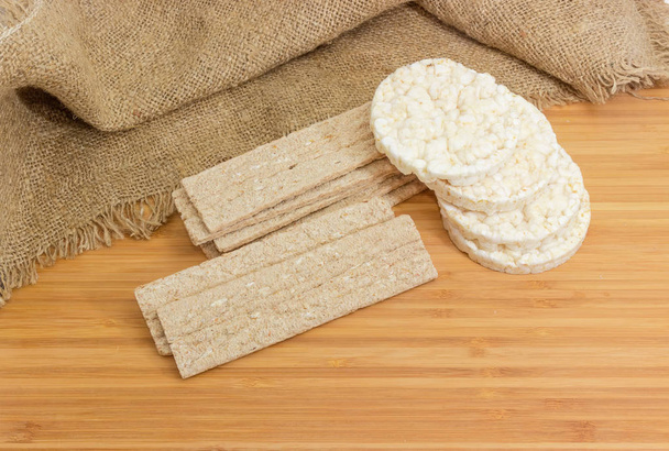 Сухий прямокутний плоский житньо-пшеничний хрусткий хліб і круглий рисовий хрусткий хліб на дерев'яній бамбуковій поверхні
 - Фото, зображення