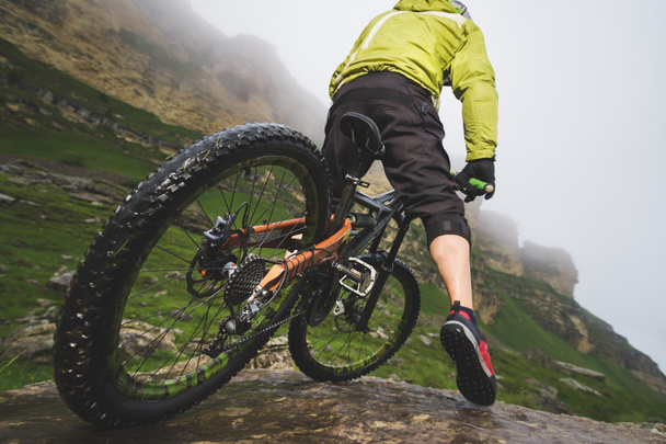 Nohy cyklistů a zadní kolo detailní pohled zadní mtb kolo v horách proti pozadí skal v mlhavé počasí. Koncept extrémních sportů - Fotografie, Obrázek