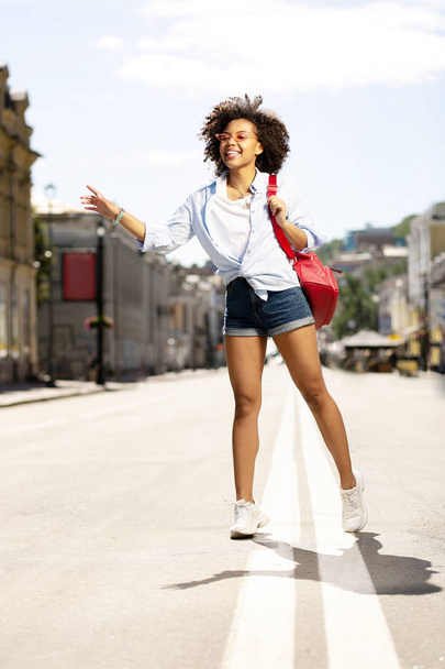 Cheerful curly woman having walk in city center - Zdjęcie, obraz