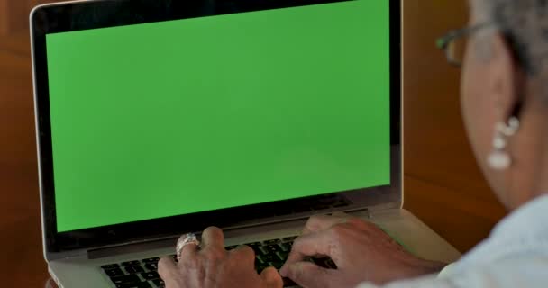 Elderly black woman typing on laptop with a green screen chroma key background - Footage, Video