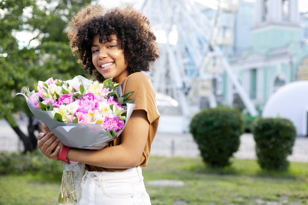 Charming curly woman posing with a big bouquet of flowers - Фото, зображення
