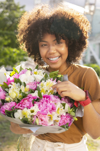 Pretty curly woman showing her bouquet of flowers - Zdjęcie, obraz