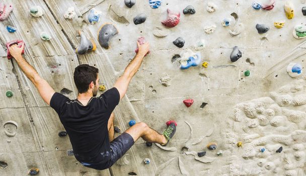 Un hombre practicando escalada en roca en paredes artificiales en interiores. Estilo de vida activo y concepto de bouldering
. - Foto, Imagen