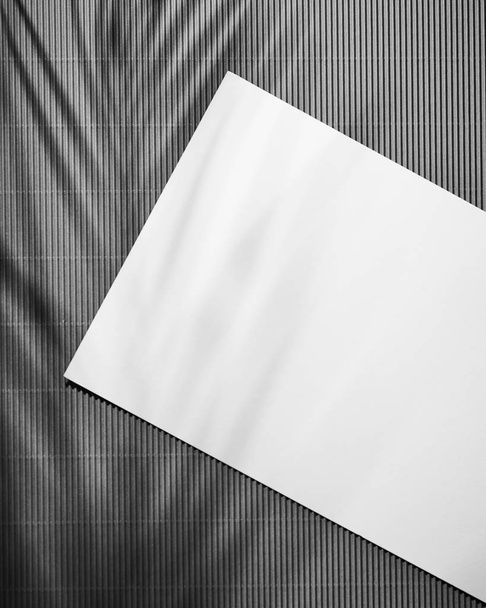 Blank sheet of paper on dark wooden table background with leaves shadows . White paper with plenty of copy space. Top view. - Фото, зображення