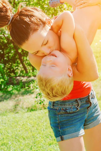 Щаслива молода брюнетка мати і син на відкритому повітрі в парку в сонячний весняний день. Молода спортивна мати піднімає сина в парку, насолоджуючись материнством
. - Фото, зображення