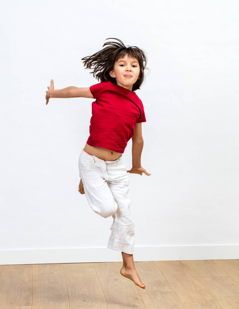 happy beautiful young girl jumping with positive energy, flying high to express joyful success, dynamic childhood and fun sports over wooden floor, white background - 写真・画像