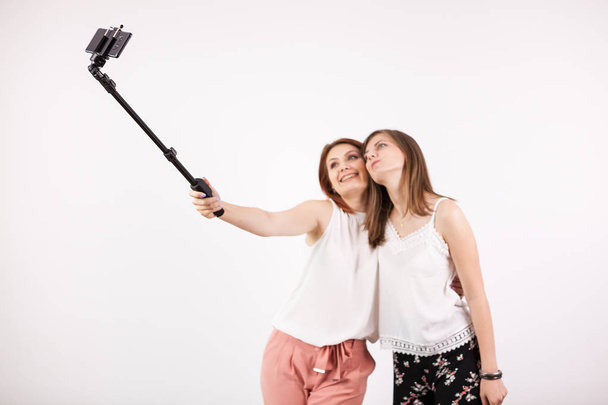 Két gyönyörű fiatal nő vesz egy selfie, egy selfie-bottal - Fotó, kép
