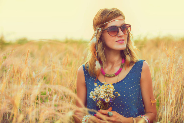 mooie vrouw in zonnebril wildflower boeket te houden terwijl u ontspant in gerst weide  - Foto, afbeelding