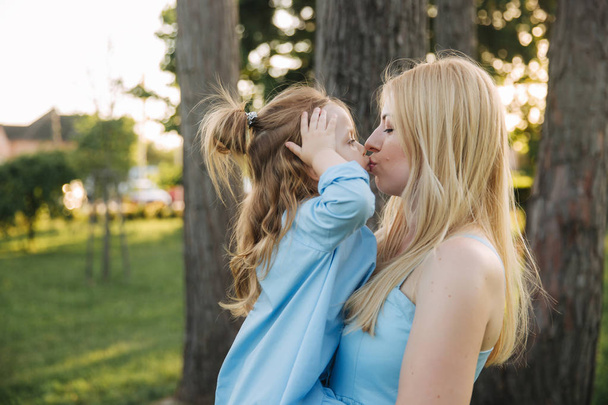 小さなかわいい娘と若い美しい女性。若い娘は、夏の公園で母親を抱擁します。 - 写真・画像