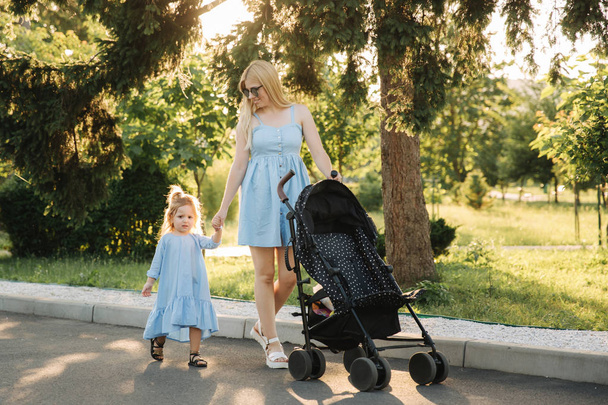 little daughter helps mom push the baby carriage - Photo, Image