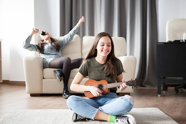 Two sisters, the younger one is playing a small guitar in front at the other is singing in the back - Photo, Image