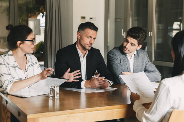 Business, career and placement concept - three executive directors or head managers sitting at table in office and discussing work with new personnel during interview - Photo, image