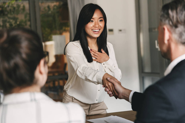 Бизнес, карьера и цементная концепция - два деловых партнера в офисе пожимают руку молодой женщине после успешных переговоров или интервью
 - Фото, изображение