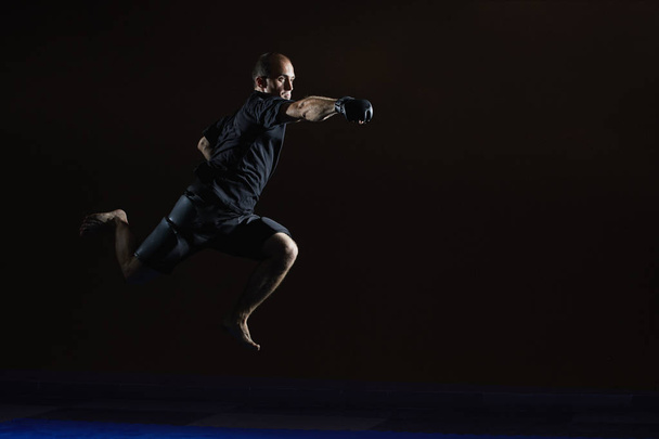 Sportler in schwarzen Handschuhen schlägt beim Sprung mit der Hand - Foto, Bild