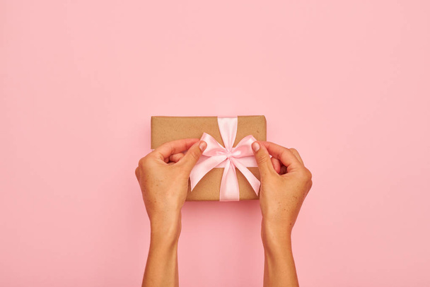 Hands tying a bow on present box on pink flatlay - Foto, Imagen