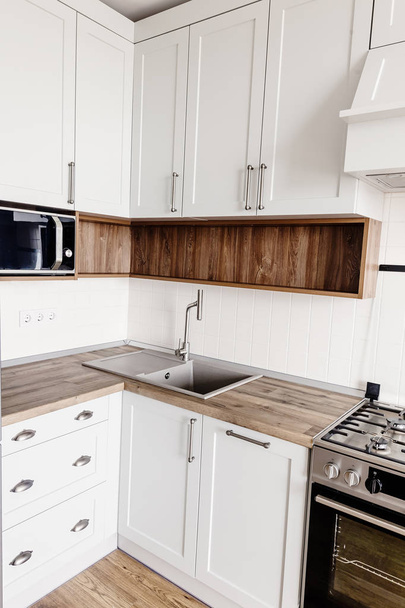 Diseño de cocina en estilo escandinavo moderno. elegante interior de cocina gris claro con muebles modernos y electrodomésticos de acero inoxidable en una casa nueva. encimera de madera, estufa de acero, fregadero y grifo
 - Foto, imagen