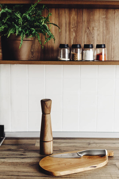 houten plank met mes, houten pepermolen op moderne keuken countertop en plank met kruiden en planten. koken voedsel. Stijlvolle keuken interieur in Scandinavische stijl - Foto, afbeelding
