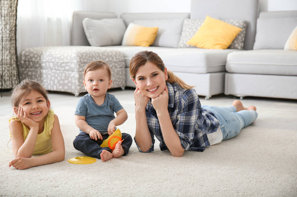 Mother with cute little children lying on cozy carpet at home - Foto, Imagen
