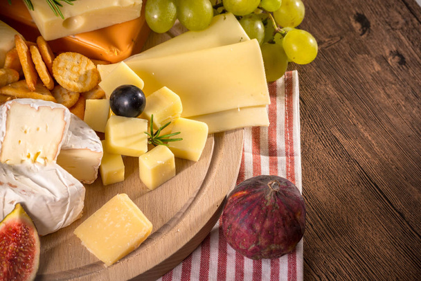 Assorted cheeses on round wooden board plate Camembert cheese, cheese grated bark of oak, hard cheese slices, walnuts, grapes, crackers, bread, thyme, wood background.Top view - Fotoğraf, Görsel