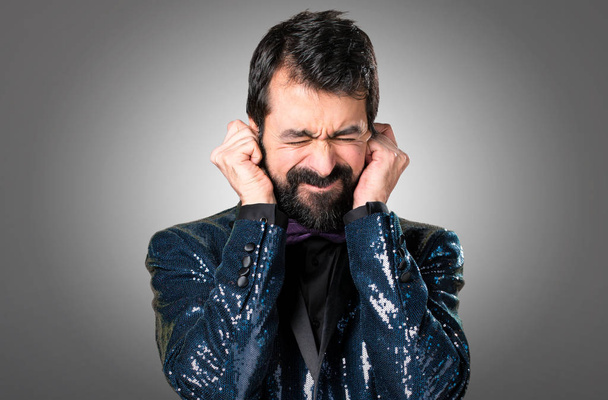 Handsome man with sequin jacket covering his ears on grey background - Foto, Imagen