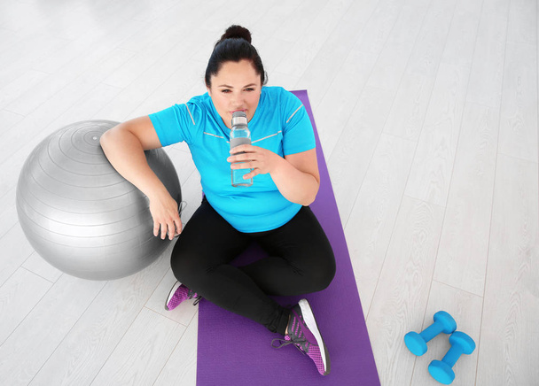 Tired overweight woman drinking water in gym - Zdjęcie, obraz