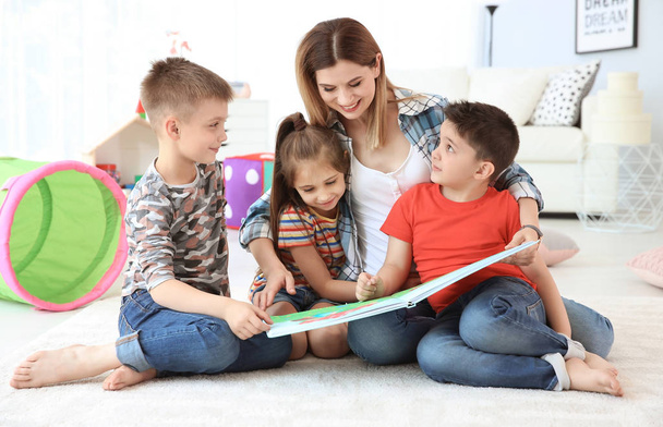 Cute little children reading book on floor with young mother in playing room - Zdjęcie, obraz