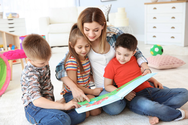 Cute little children reading book on floor with young mother in playing room - Photo, Image