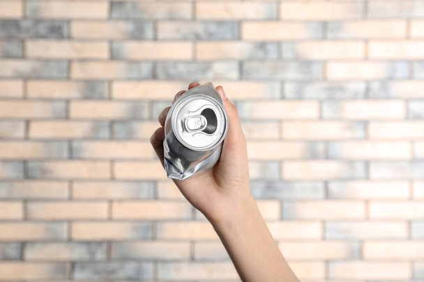 Woman holding crumpled aluminum can on brick wall background. Metal waste recycling - 写真・画像