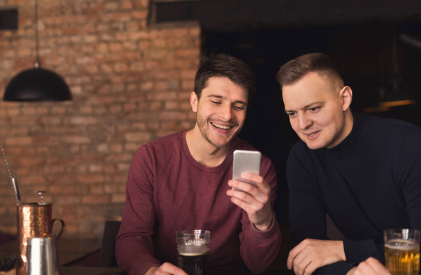 Ystävät nauttivat tuoretta olutta pubissa ja jakavat mobiili
 - Valokuva, kuva